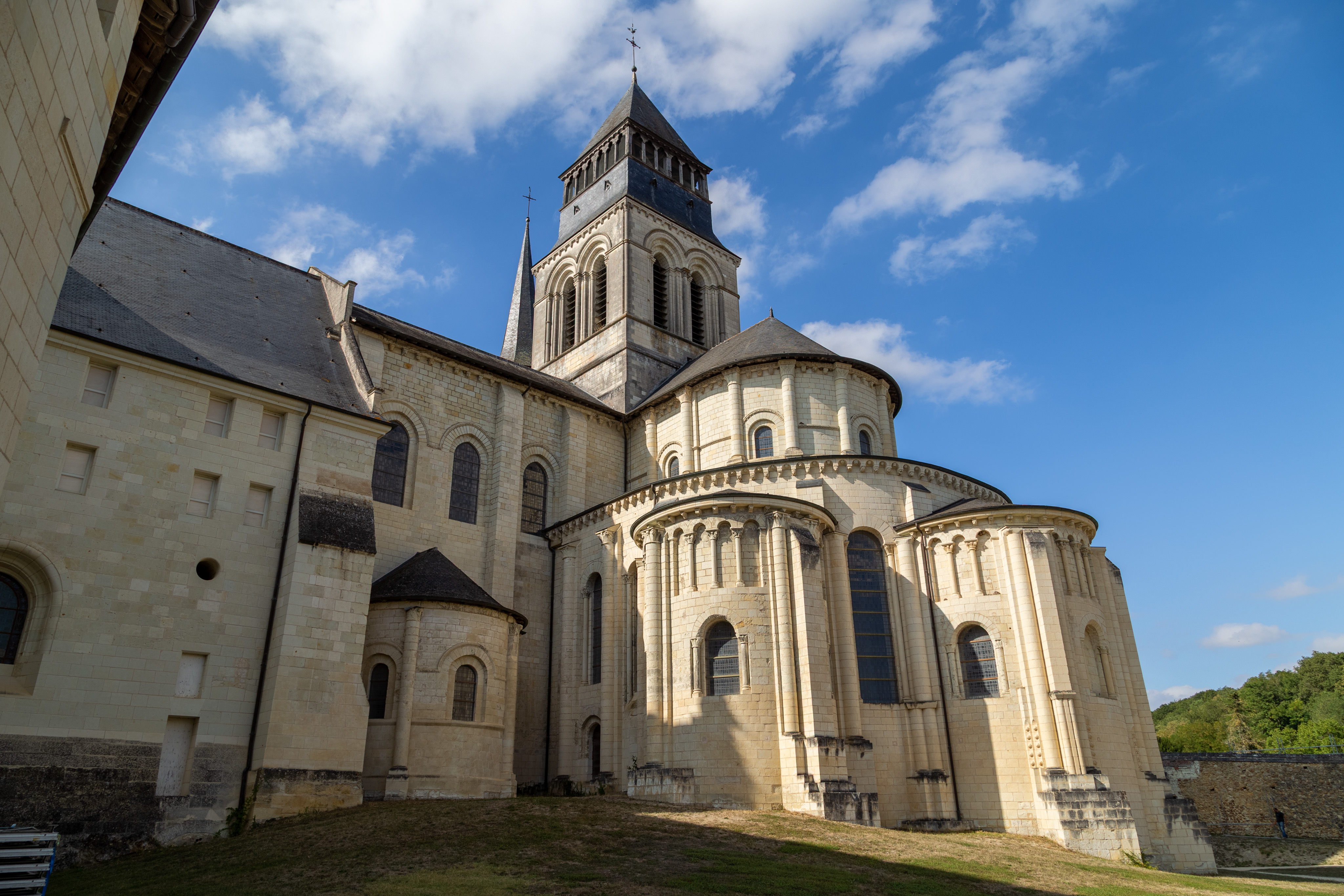 A view of the rear (alter side) of the Fontevraud Abbey. The building itself is white stone with a black roof in a romanesque style. The sky is deep blue with a handful of clouds.