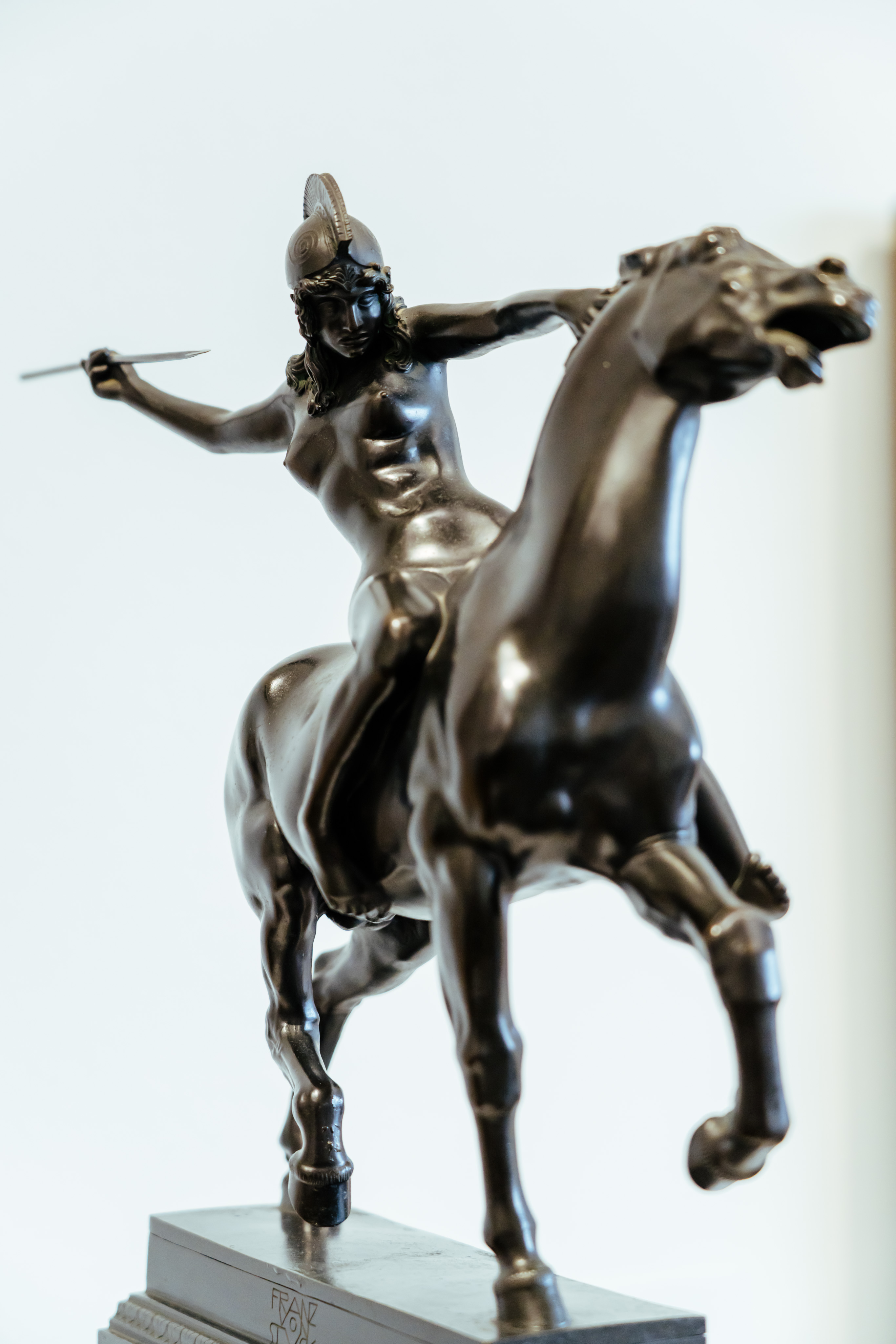 A black statue of a woman riding a horse. The woman is nude and holding a javelin posed right before she throws the javelin. She is wearing a helmet and the horse looks startled. On the pedestal, one can just make out the engraving "franz"