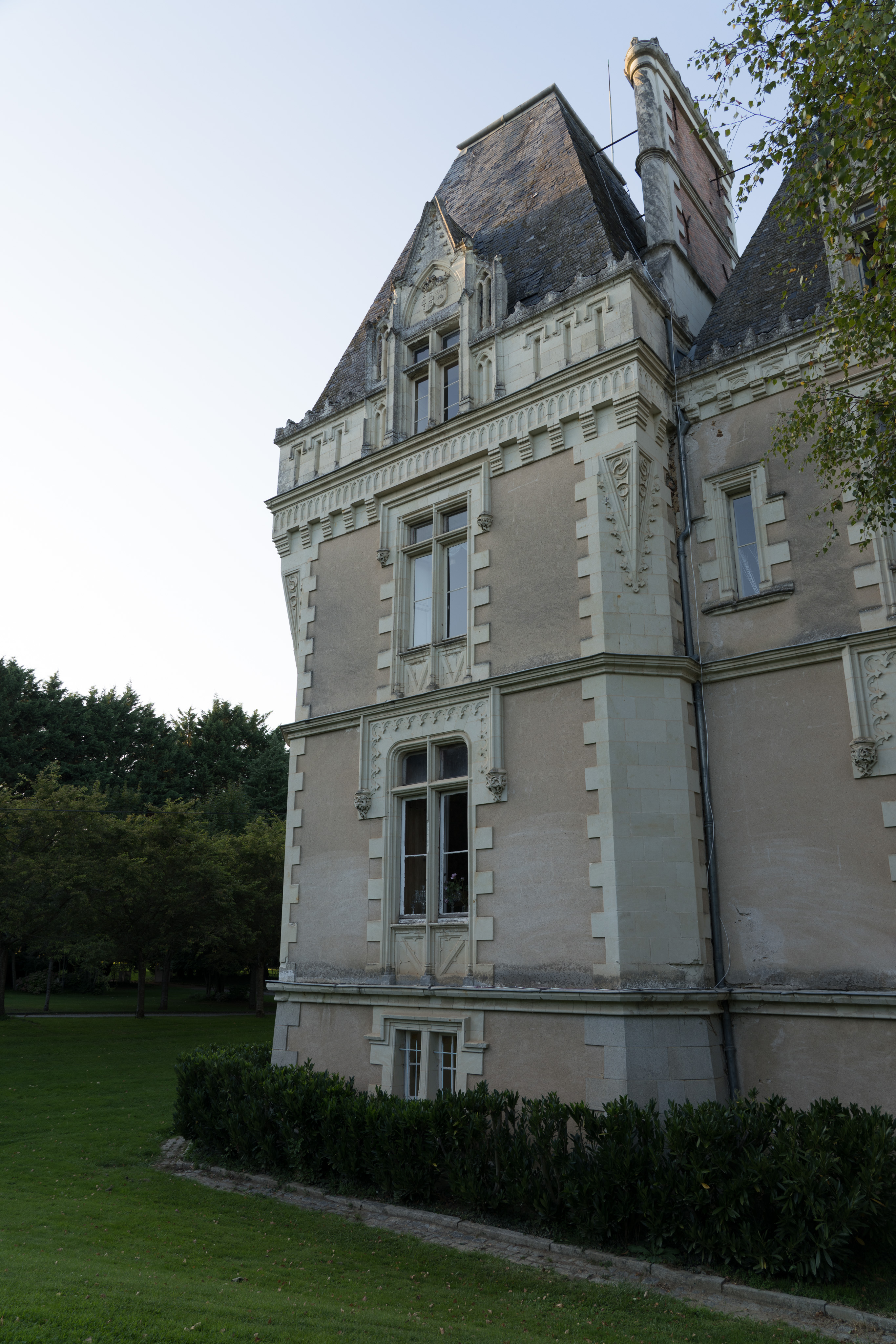 One side of the château. The outside walls are white and grey stones, on each level are rectangular windows. There are a number of ornate decorative stone work in the corners and where the roof meets the walls