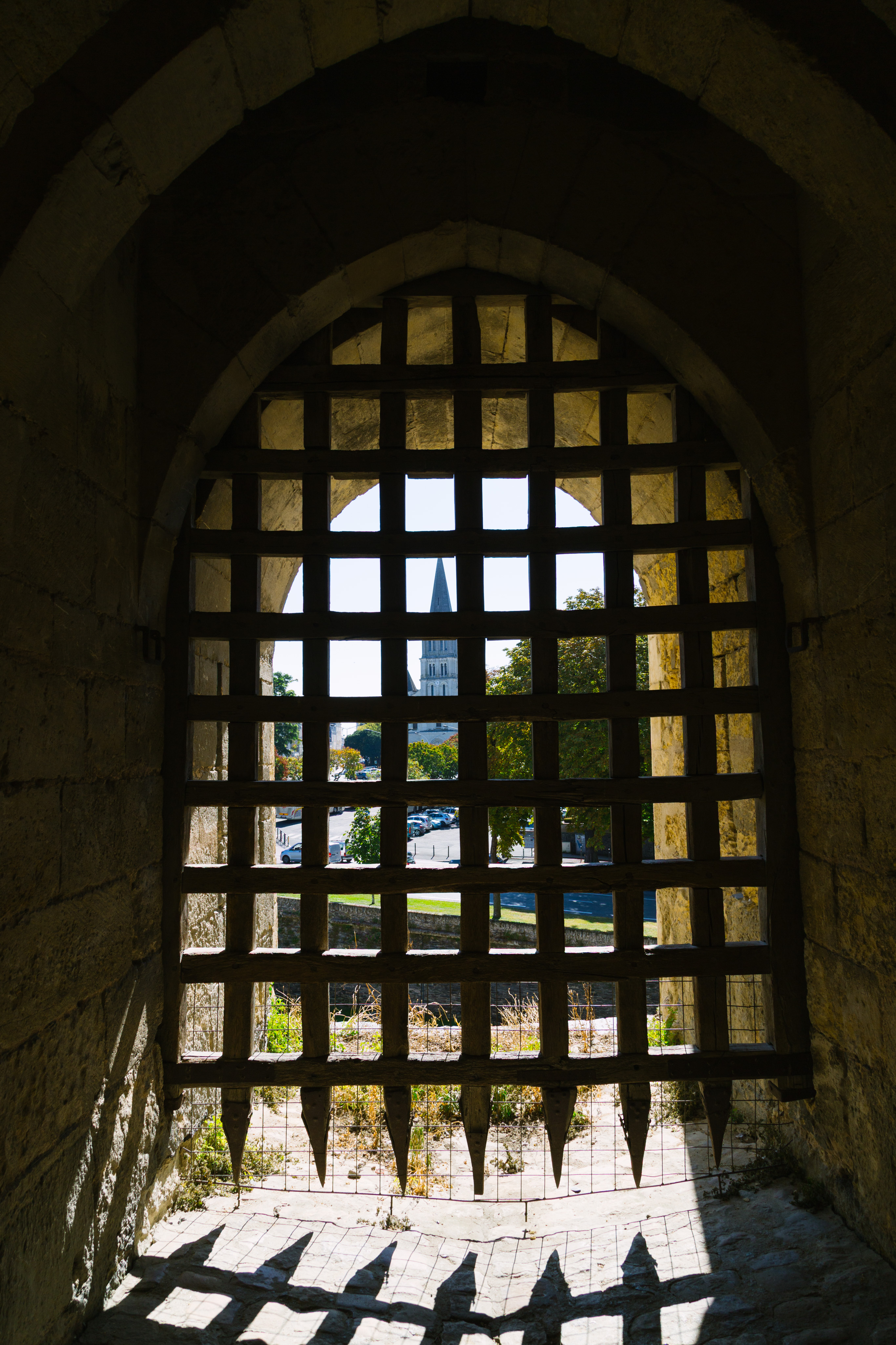 A view through a large portcullis. Behind the portcullis a street and cathedral can be seen.