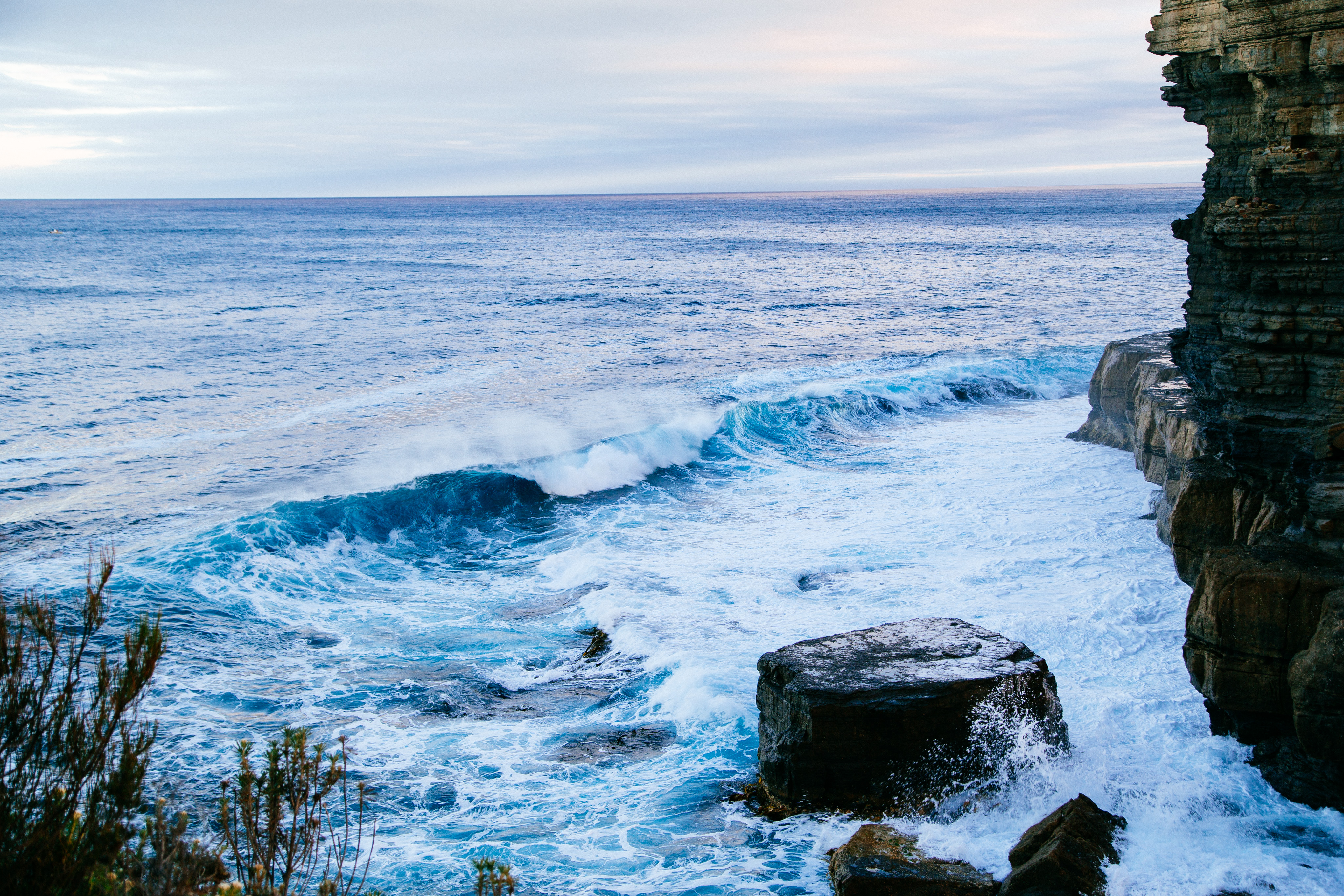 A wave crashes towards a rocky cliff.