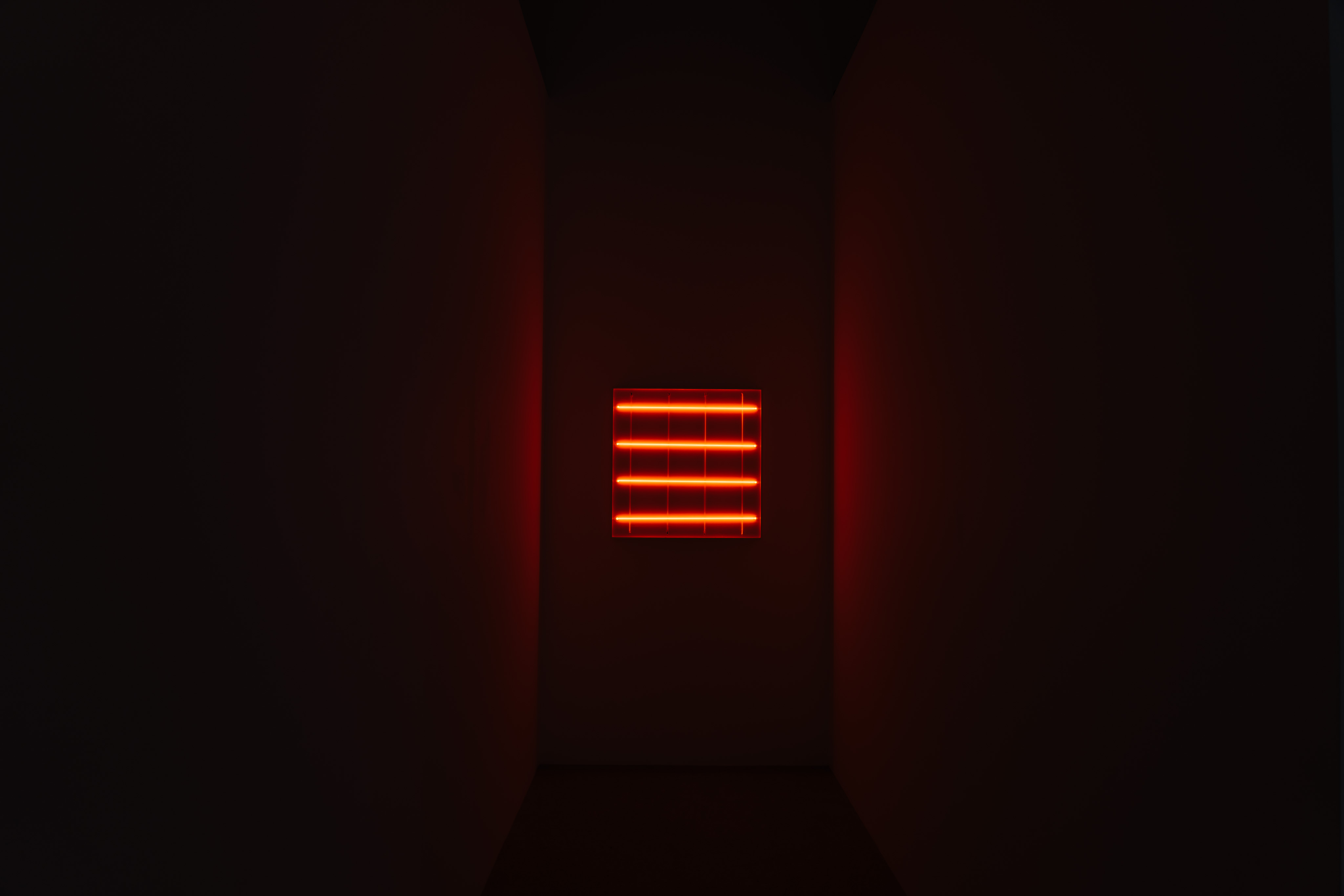 A piece of contemporary art hanging at the end of a hallway. The art itself is four illuminated red neon tubes. There are four more not-illuminated neon tubes below and orthogonal to the lighted tubes.