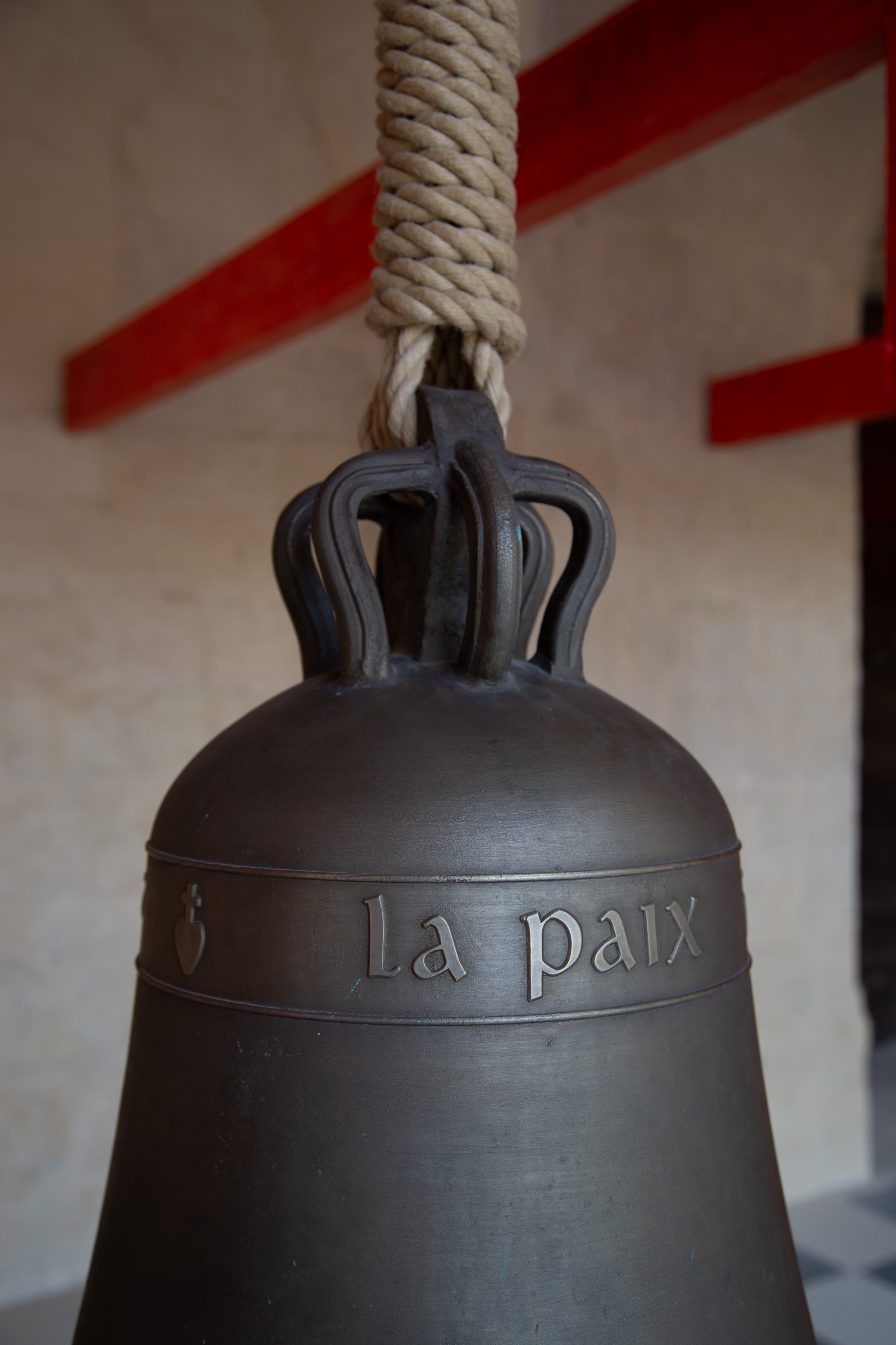 The top of a large decorative bell. It us hung by a large rope. On the bell are the words "La Paix"