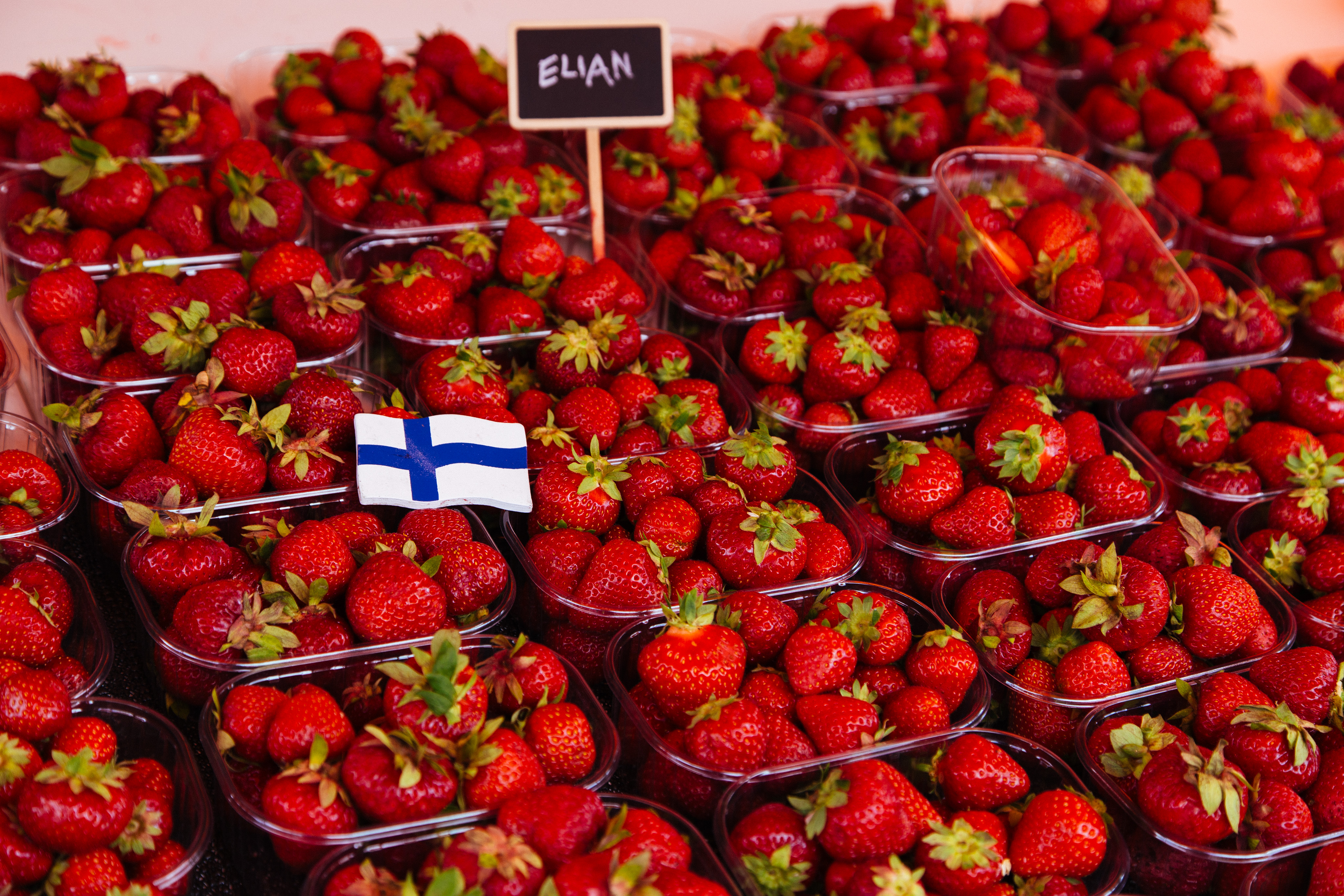 Small cartons of strawberries aligned in rows. A small wooden Finnish flag rests on top, and a small sign in the back says "elian".