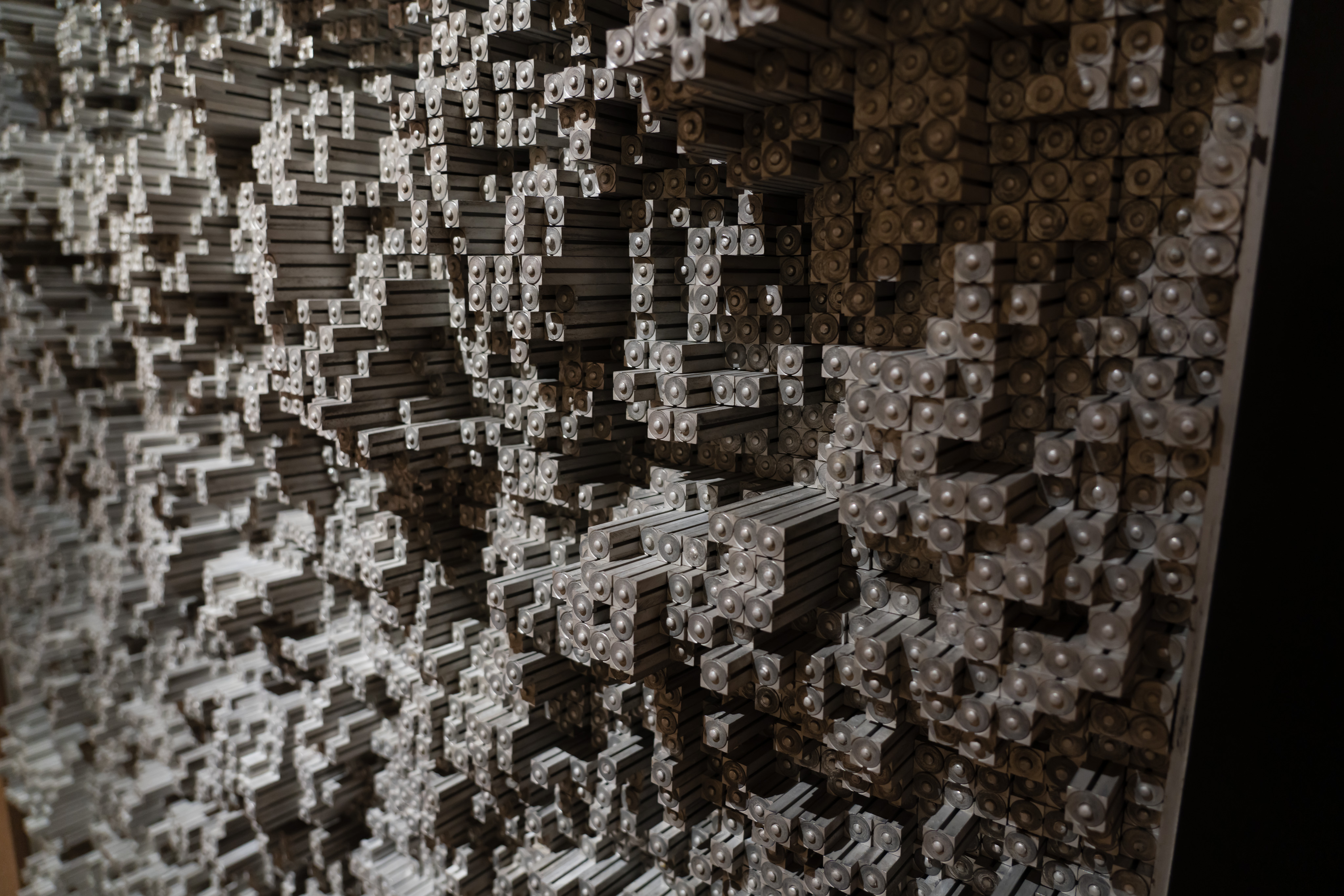 An art piece made of a large number of small square metal rods. Each rod has a circle and a small nub protruding from the end. Each rod is at a different depth creating a topography of hills, mountains, and valleys.
