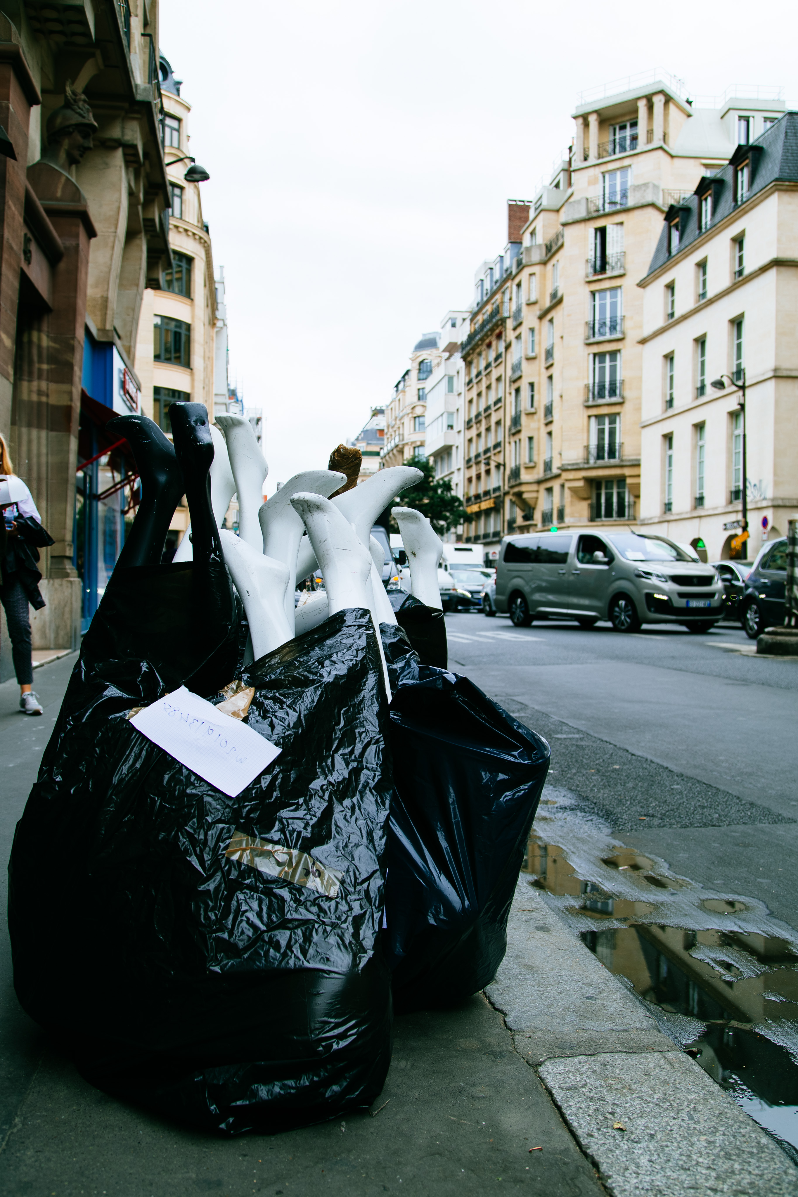 A number of black and white mannequin legs and feet stuffed into large plastic trash bags sit on a street in Paris.