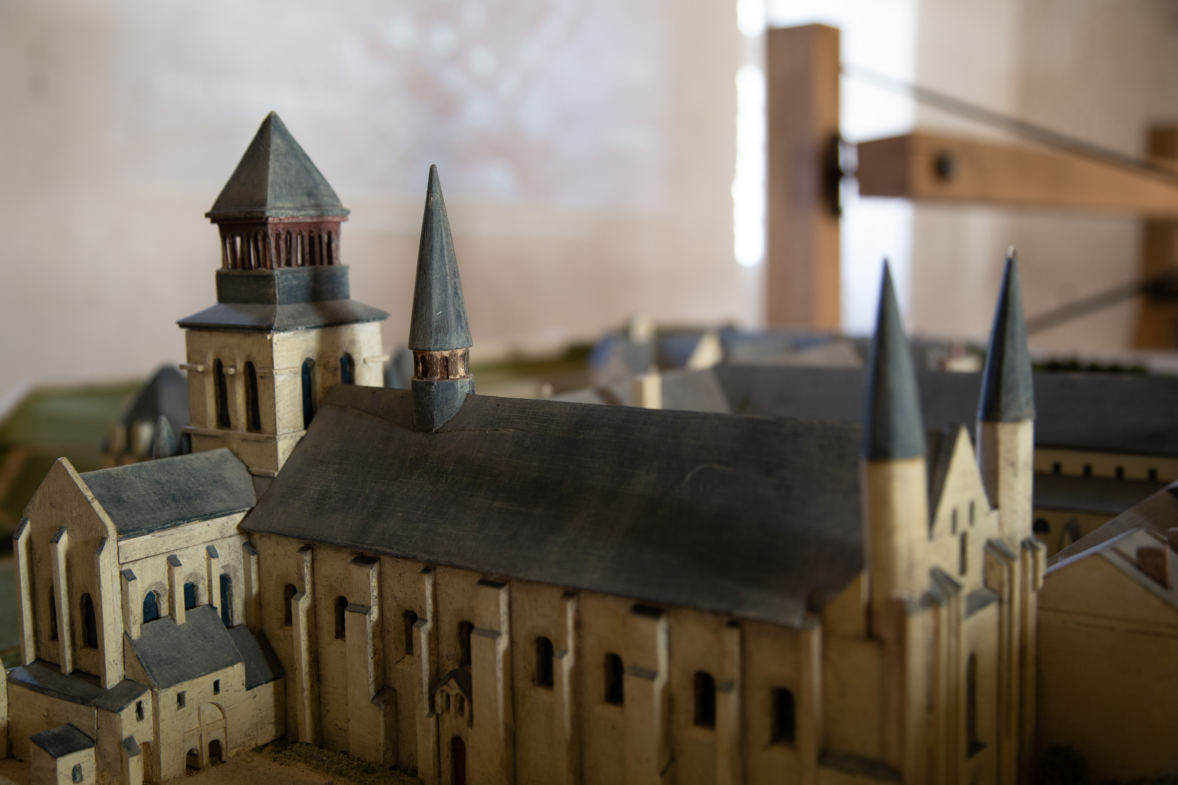 A small model of the Fontevraud Abbey. The walls of the building are white and the roof black. The focus is the main abbey building, two pointed towers are at the front, and one is just before where the transepts are. One last square tower stands where the transepts intersect.