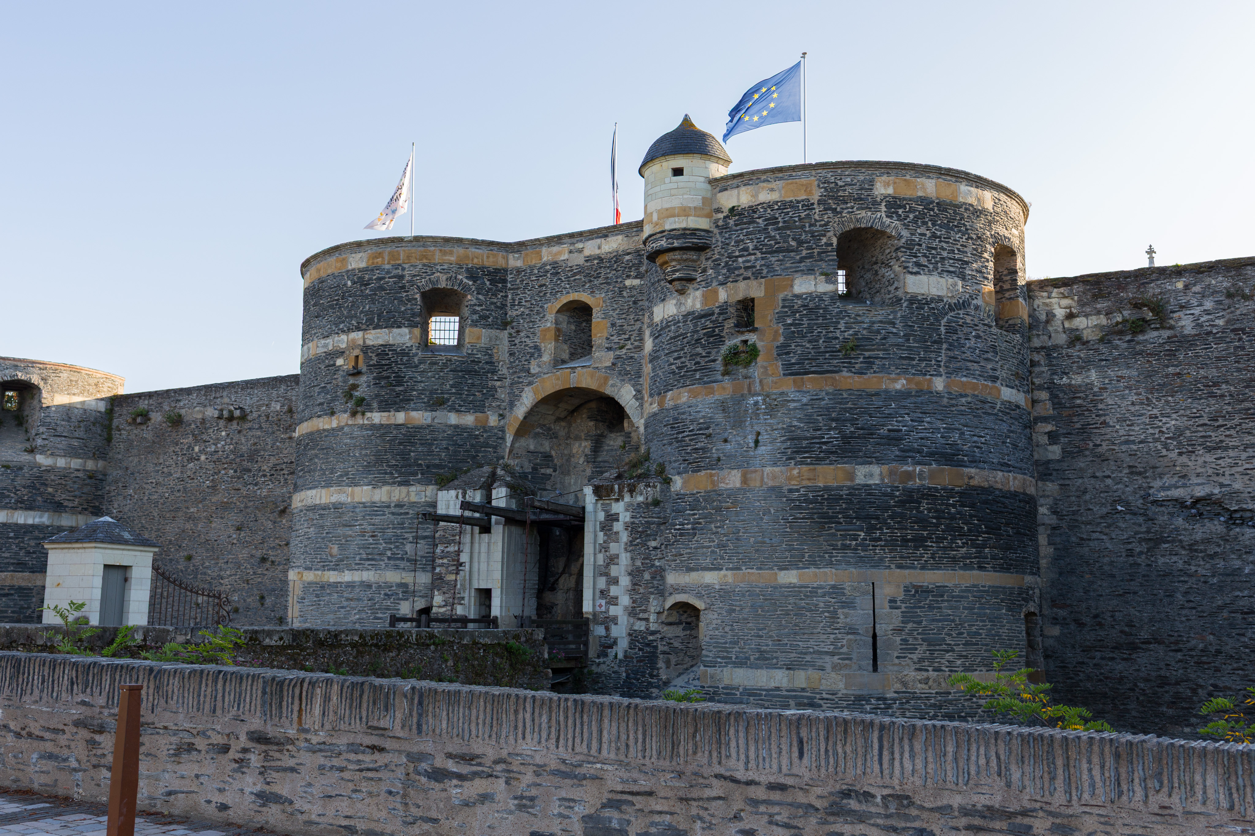 A view of the front gate of the Château d'Angers. Three flags are flying on top, the only one visible is the flag of the EU.