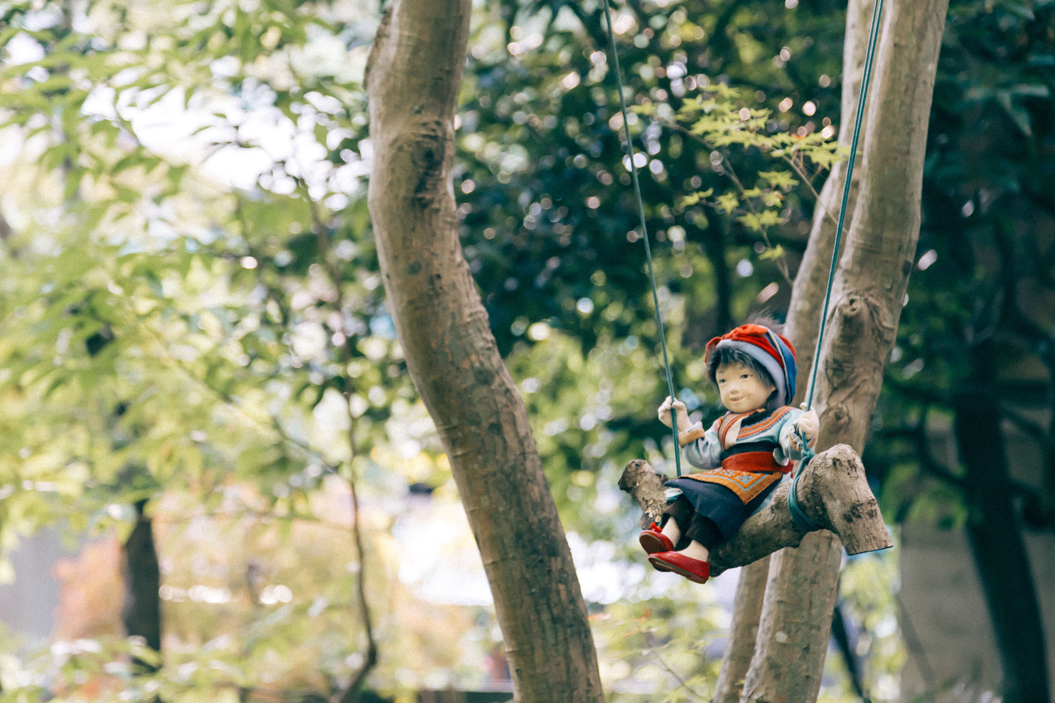 A doll sits on a home-made swing in the middle of a wooded area.